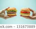 Hands hold two different types of burgers, one with patty and the other vegetarian in bright setting 131673889