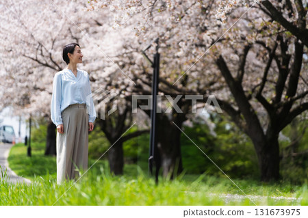 A young woman walking along a row of cherry blossom trees. Lifestyle image A young woman walking along a row of cherry blossom trees. Lifestyle image 131673975