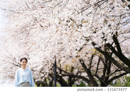 A young woman walking along a row of cherry blossom trees. Lifestyle image A young woman walking along a row of cherry blossom trees. Lifestyle image 131673977