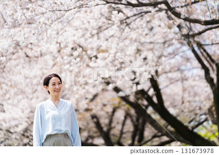 A young woman walking along a row of cherry blossom trees. Lifestyle image A young woman walking along a row of cherry blossom trees. Lifestyle image 131673978