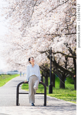 A young woman posing under a row of cherry blossom trees. Lifestyle image A young woman posing under a row of cherry blossom trees. Lifestyle image 131674017