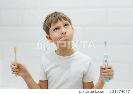 cute 8 years old boy holding bamboo and electric tooth brush making choice 131674077
