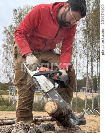 A man cutting a log into firewood using a chainsaw 131674106
