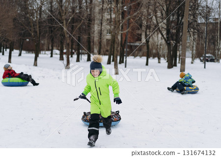 boy running with snow tubing in park . Winter family activities concept. boy running with snow tubing in park . Winter family activities concept. 131674132