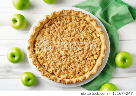 Delicious homemade apple pie with golden crust surrounded by fresh apples and green leaves on rustic white wooden background. Perfect autumn dessert or bakery product presentation. Copy space. Banner 131674247