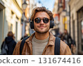 Young man enjoys music in headphones while walking through bustling city street on sunny day, showcasing his relaxed style and enjoyment of urban life 131674416