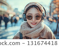 Young woman smiles while wearing stylish headphones and sunglasses in a bustling urban setting during daytime in winter 131674418