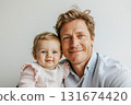 Joyful father holds his smiling baby daughter during a close-up portrait session at home in soft afternoon light 131674420