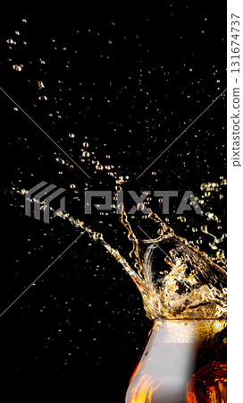 Golden whiskey splash with flying droplets in dark studio Golden whiskey splash with flying droplets in dark studio 131674737