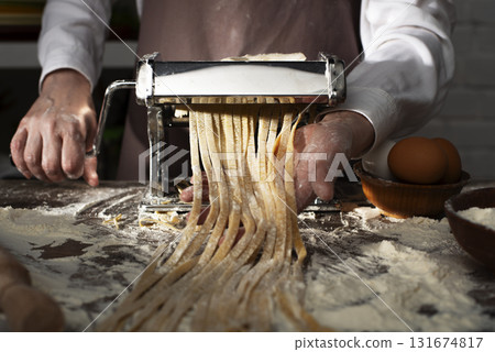 Caucasian female hands making fettuccine noodles using mechanical pasta machine 131674817