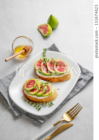 Toasts with fresh figs, cheese, thyme, and honey on a light background. 131674823