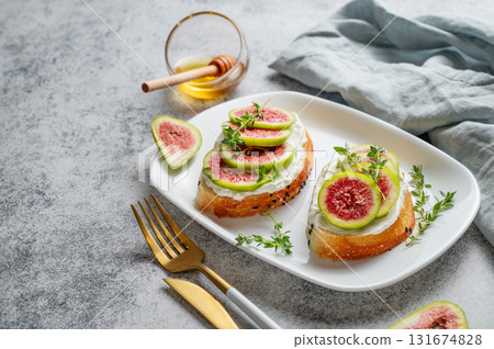 Sweet toasts with fresh figs, cheese, thyme, and honey on a gray background close up. Sweet toasts with fresh figs, cheese, thyme, and honey on a gray background close up. 131674828