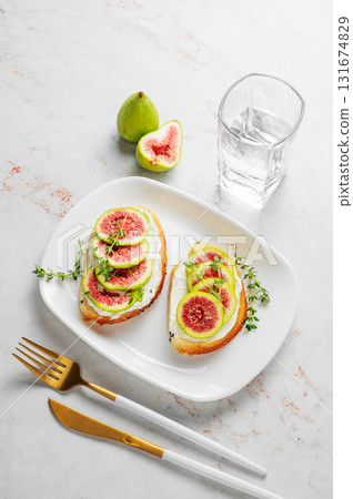 Sweet toasts with fresh figs, cream cheese, thyme, and honey on a marble background. Sweet toasts with fresh figs, cream cheese, thyme, and honey on a marble background. 131674829