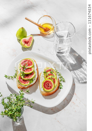 Sweet toasts with fresh figs, cream cheese, thyme, and honey on a marble background. 131674834