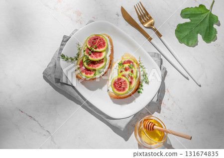 Sweet toasts with fresh figs, cream cheese, thyme, and honey on a marble background. 131674835