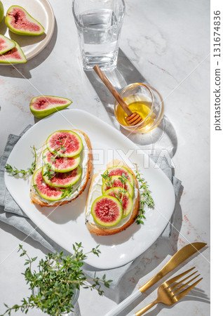 Sweet toasts with fresh figs, cream cheese, thyme, and honey on a marble background. Sweet toasts with fresh figs, cream cheese, thyme, and honey on a marble background. 131674836