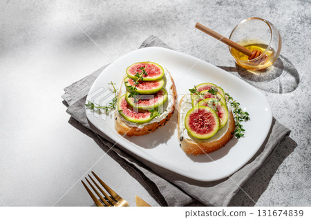 Sweet toasts with fresh figs, cream cheese, thyme, and honey on a gray background. 131674839