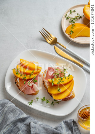 Bruschetta with peach, cream cheese, prosciutto and honey on a plate on a light background 131674841