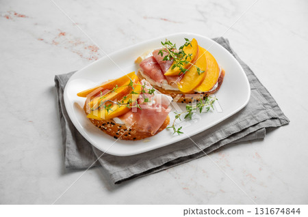 Sandwich with peach, cream cheese, prosciutto and honey on a plate on a marble background with thyme 131674844