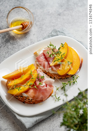 Toast with peach, cream cheese, ham and honey on a plate on a gray background with thyme close up. Toast with peach, cream cheese, ham and honey on a plate on a gray background with thyme close up. 131674846