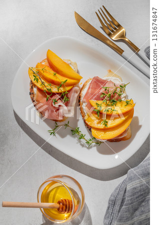 Bruschetta with peach, cream cheese, prosciutto and honey on a plate on a light background Bruschetta with peach, cream cheese, prosciutto and honey on a plate on a light background 131674847