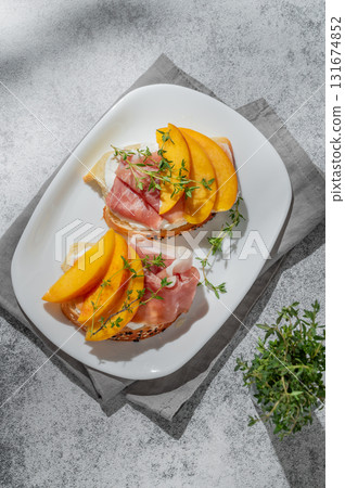 Sandwich with peach, cream cheese, prosciutto and honey on a plate on a gray background Sandwich with peach, cream cheese, prosciutto and honey on a plate on a gray background 131674852