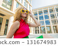 Young blonde woman with long curly hair in red and green closes in sun glasses playful smile happy positive 131674983