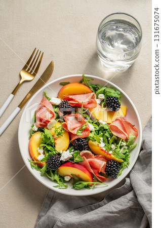 Fresh salad with peaches, arugula, feta, prosciutto and berries in a plate on a light background 131675074