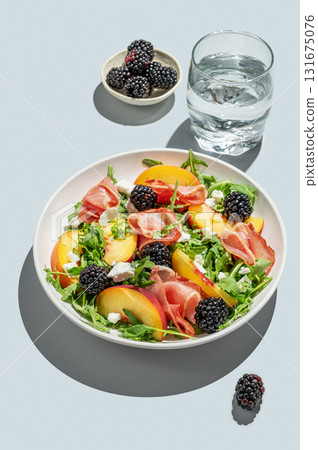 Salad with peaches, arugula, feta, prosciutto and berries in a plate on a blue background Salad with peaches, arugula, feta, prosciutto and berries in a plate on a blue background 131675076