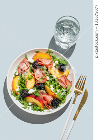 Salad with peaches, arugula, feta, prosciutto and berries in a plate on a blue background 131675077
