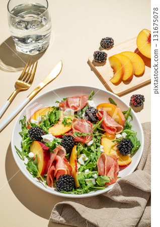 Salad with peaches, arugula, feta, prosciutto and berries in a plate on a yellow background 131675078