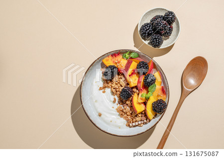 Natural greek yogurt with granola or muesli, peach and blackberry in a bowl on a beige background Natural greek yogurt with granola or muesli, peach and blackberry in a bowl on a beige background 131675087