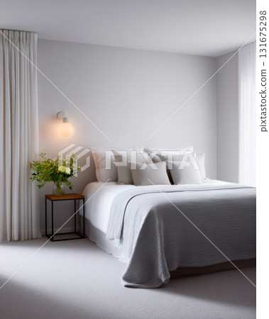 Calm and serene minimalist bedroom interior with comfortable bed, soft pillows, and cozy grey blanket. warm lamp provides soft light next to elegant white curtain 131675298
