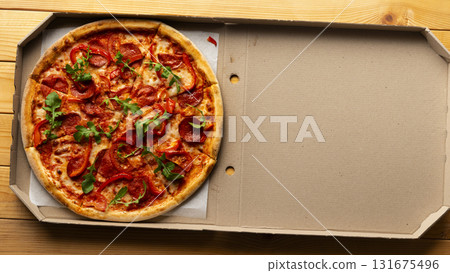Pepperoni pizza with bell peppers and arugula in open carton box on natural wooden kitchen table flat lay with copy-space Pepperoni pizza with bell peppers and arugula in open carton box on natural wooden kitchen table flat lay with copy-space 131675496