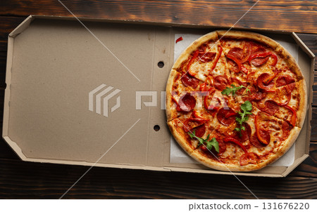 Pepperoni pizza with bell peppers and arugula in open carton box on dark wooden table flat lay with copy-space Pepperoni pizza with bell peppers and arugula in open carton box on dark wooden table flat lay with copy-space 131676220