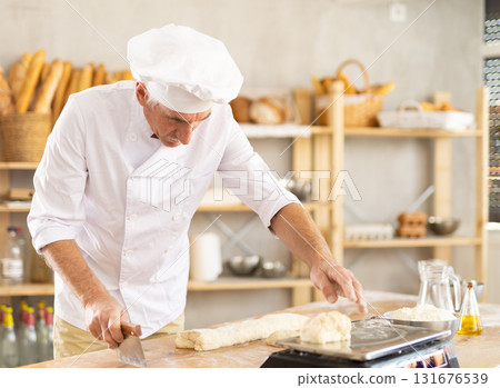 Elderly man baker weighs pieces of dough 131676539