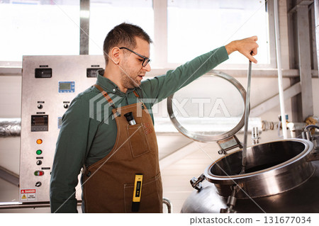 Brewer stirring liquid in large vat during craft beer production 131677034