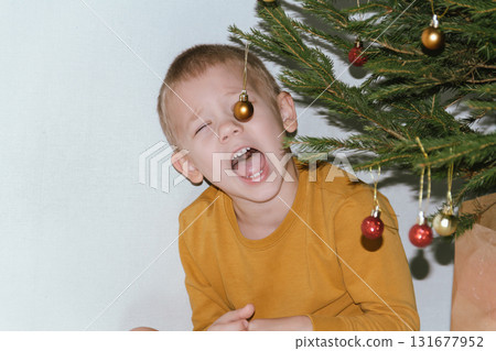 Festive baby boy in yellow sweater getting ready to decorate the Christmas tree, creating a warm holiday atmosphere for celebrating with loving family members tonight. 131677952