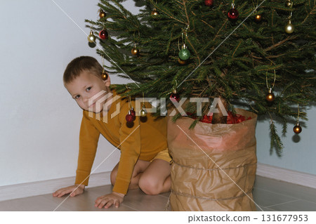 Festive baby boy in yellow sweater getting ready to decorate the Christmas tree, creating a warm holiday atmosphere for celebrating with loving family members tonight. Festive baby boy in yellow sweater getting ready to decorate the Christmas tree, creating a warm holiday atmosphere for celebrating with loving family members tonight. 131677953