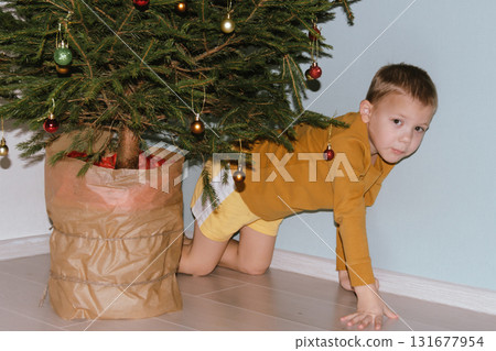 Festive baby boy in yellow sweater getting ready to decorate the Christmas tree, creating a warm holiday atmosphere for celebrating with loving family members tonight. 131677954