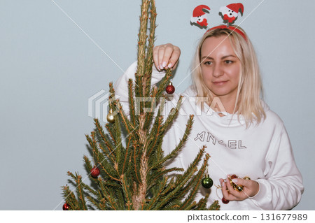 Beautiful young woman wearing knitted sweater and woolen hat standing near red car with Christmas tree on the top under snowfall. Happy winter holidays 131677989