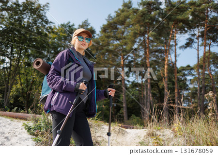 Female trekker walking near forest edge with poles 131678059
