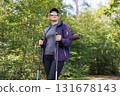 Confident female hiker with trekking poles walking on forest path 131678143
