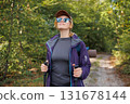 Smiling woman in sunglasses hiking with poles in green forest 131678144