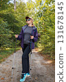 Young woman in sportswear enjoying forest hike with trekking poles 131678145