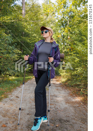 Young woman in sportswear enjoying forest hike with trekking poles 131678145