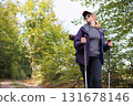 Adventurous woman walking with trekking poles on sunny forest path 131678146