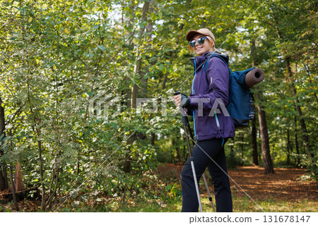 Smiling hiker with backpack and trekking poles in summer forest 131678147