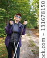 Smiling woman with trekking poles enjoying hiking in forest nature 131678150
