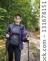 Smiling woman hiker with trekking poles walking in forest trail 131678151